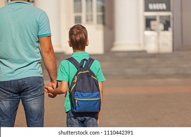 Cute Little Boy With Backpack Going To School With His Father. Back View