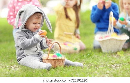 Cute Little Boy With Basket On Green Grass In Park. Easter Egg Hunt Concept