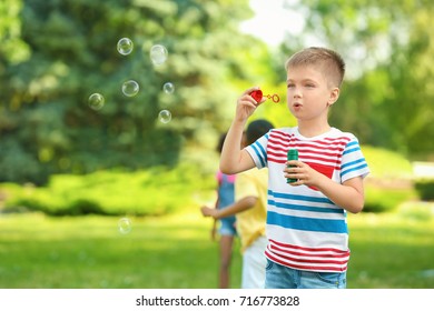 Cute little boy blowing soap bubbles outdoors