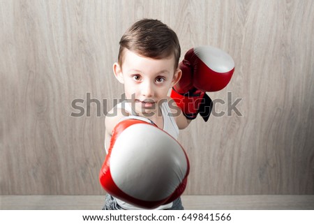 cute little boy with boxing gloves large size. Portrait of a sporty child engaged in box. fooling around and not serious. wooden background