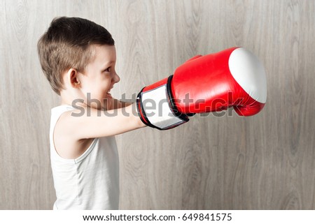 cute little boy with boxing gloves large size. Portrait of a sporty child engaged in box. fooling around and not serious. wooden background