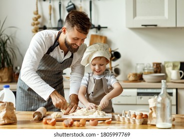 Pequeño chico lindo con sombrero de chef y manto amasando masa con la ayuda de su padre mientras preparaba el pastel juntos en la acogedora cocina de casa
