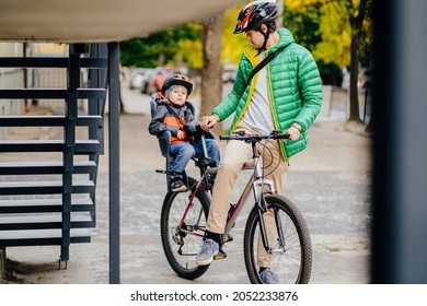 Cute Little Boy In Child Seat To Ride A Bicycle With His Father In City Street. Father Walking With His Son Cycling At Autumn Time Outdoor.