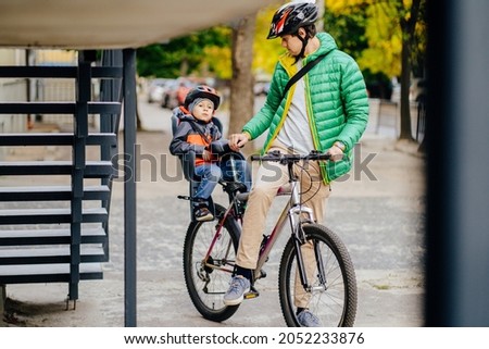 Cute little boy in child seat to ride a bicycle with his father in city street. Father walking with his son cycling at autumn time outdoor.