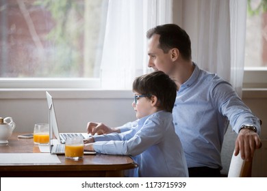 Cute Little Boy Copy Dad Behavior Working At Laptop, Parent And Child Sit Together In Kitchen Using Computers, Father And Son Have Fun Enjoy Time, Small Funny Kid Act Like Daddy Busy With Gadget