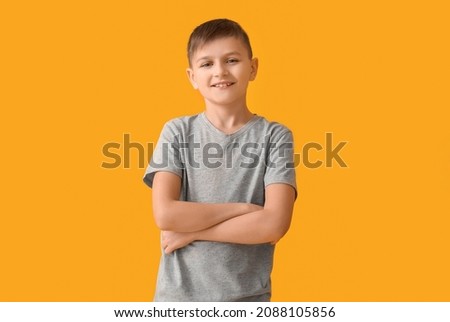 Cute little boy with crossed arms on color background