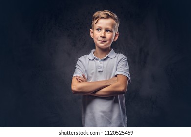 Cute little boy dressed in a white t-shirt standing with crossed arms in a studio. Isolated on dark textured background.