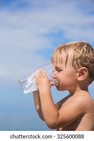 Cute Little Boy Is Drinking Clean Water From A Plastic Cup Outside The House On A Background Of Blue Sky