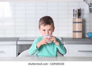 Cute Little Boy Drinking Milk At Table In Kitchen