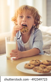 Cute Little Boy Is Drinking Milk And Eating Cookies While Sitting On Couch At Home