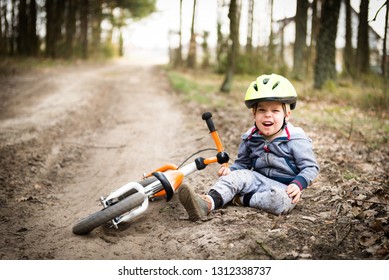 Cute little boy fallen off his bicycle outdoors, but he's feel ok, don't cry, he's all good. He is looking at camera and be a little vexed. Concept of sport and safety, kids ride bicycle; first bike; 