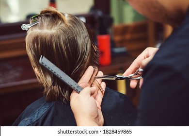 Cute little boy getting haircut by hairdresser at the barbershop. Barber man doing kid the hairstyle. Hairdresser with scissors. Barber shop. Childhood. New hairstyle for young boy.