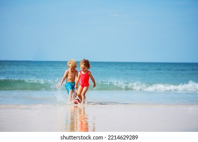 Cute little boy and a girl play with the ball in the ocean waves at the sand beach during summer vacation - Powered by Shutterstock