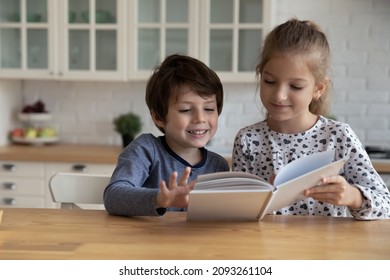 Cute little boy and girl reading fairy tale book together, sitting at table, smiling adorable 5s brother and 8s sister, siblings engaged in educational activity, having fun, spending leisure time