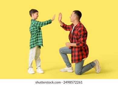 Cute little boy giving high-five to his father on yellow background - Powered by Shutterstock