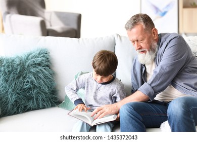 Cute little boy with grandfather reading book at home