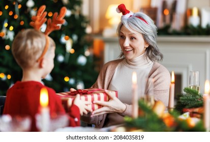 Cute little boy grandson giving wrapped holiday Christmas gift to smiling senior grandmother during festive Xmas dinner, family celebrating New Years Eve at home. Winter holiday concept - Powered by Shutterstock