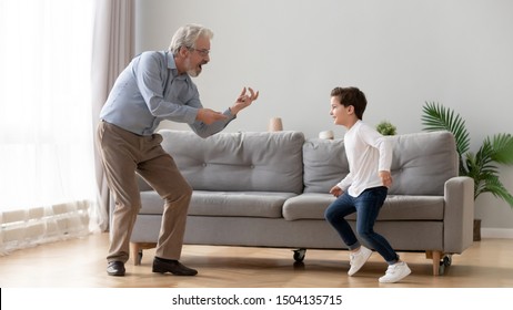 Cute Little Boy Grandson Having Fun Dancing With Old Elderly Grandpa In Living Room, Happy Two Generation Active Family Senior Grandfather And Small Grandchild Playing Enjoying Time Together At Home