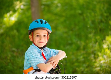 Cute Little Boy In Helmet On Bike In Forest