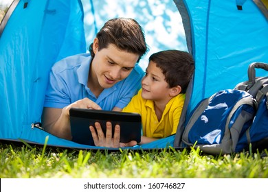 Cute Little Boy And His Dad Using A Tablet Computer And Relaxing On A Tent On A Camping Trip