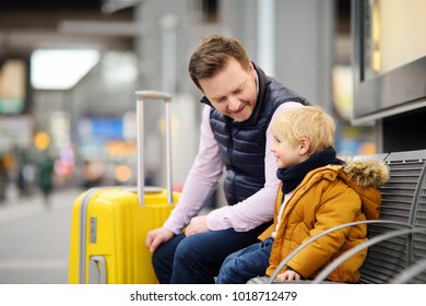 Cute Little Boy And His Father Waiting Express Train On Railway Station Platform Or Waiting Their Flight At The Airport. Travel, Tourism, Winter Vacation And Family Concept. Man And His Son Together.