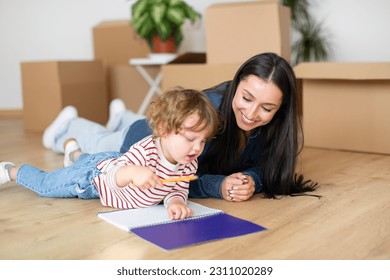 Cute Little Boy And His Mother Relaxing On Floor After Moving Home, Adorable Toddler Child Writing In Notepad And Bonding With Mom Among Cardboard Boxes With Belongings, Making Checklist Together - Shutterstock ID 2311020289
