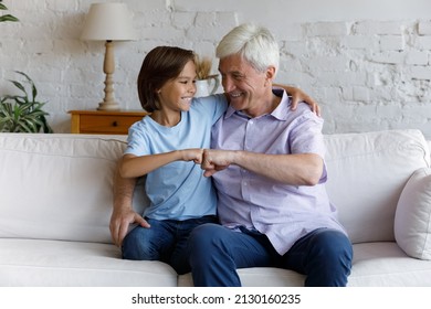 Cute little boy his older grandfather embracing seated on cozy sofa at home, making fist bumping gesture, feeling bond, express respect. Multigenerational family unity, attachment, friendship concept - Shutterstock ID 2130160235