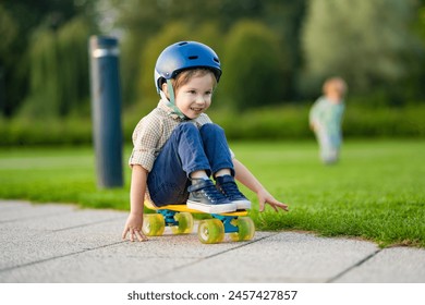 Cute little boy learning to skateboard on beautiful summer day in a park. Child wearing safety helmet enjoying skateboarding ride outdoors. Active leisure for small kids. - Powered by Shutterstock