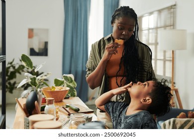 Cute little boy looking at his mother with homemade cookie having snack and chatting with her adorable son during breakfast in the kitchen - Powered by Shutterstock