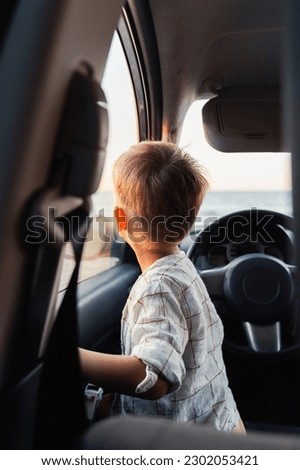 Cute little boy looking out of window of a car during sunset on the beach.