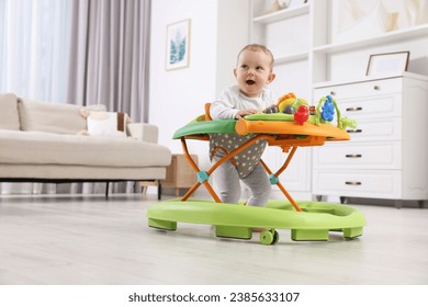 Cute little boy making first steps with baby walker at home