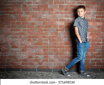 Cute Little Boy On Brick Wall Background. Kids Fashion Concept