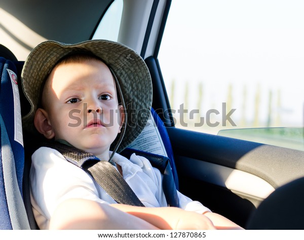 Cute little boy passenger in a car\
sitting quietly on the back seat in his child safety\
seat