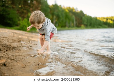 Cute little boy playing by a lake or river on hot summer day. Adorable child having fun outdoors during summer vacations. Water activities for kids. - Powered by Shutterstock