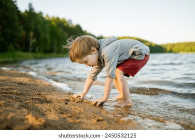 Cute little boy playing by a lake or river on hot summer day. Adorable child having fun outdoors during summer vacations. Water activities for kids. - Powered by Shutterstock