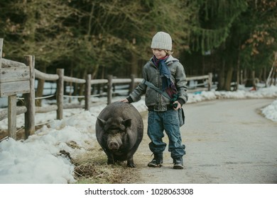 Cute little boy playing with pet pig. Raising kids around animals, positive effects of pet ownership concept. Vintage look.