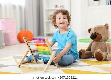 Cute little boy playing with wooden abacus on floor in kindergarten - Powered by Shutterstock