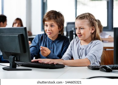 Cute little boy pointing while using desktop PC with friend at desk in school computer lab - Powered by Shutterstock