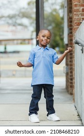 A cute little boy of preschool age with a blue shirt downtown in the city wearing denim jeans standing.