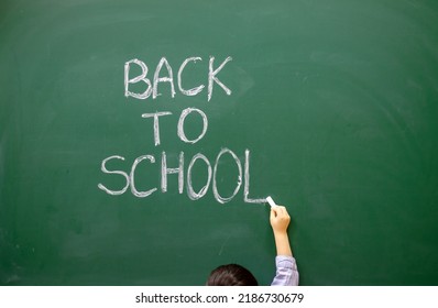 Cute Little Boy Preschooler Is Writing On Blackboard With White Chalk The Words Back To School.kid Is Wearing Funny Round Party Glasses With No Glass Inside.education,learning,classroom Interior