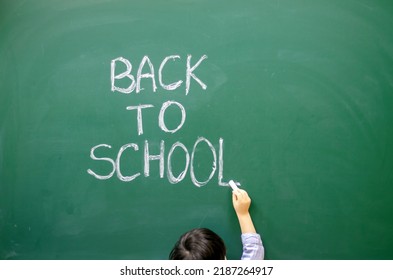 Cute Little Boy Preschooler Is Writing On Blackboard With White Chalk The Words Back To School.kid Is Wearing Funny Round Party Glasses With No Glass Inside.education,learning,classroom Interior