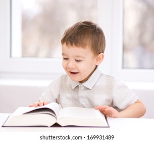 Cute little boy is reading book while sitting at table, indoor shoot - Powered by Shutterstock