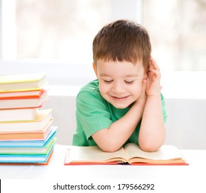 Cute little boy is reading book while sitting at table, indoor shoot - Powered by Shutterstock