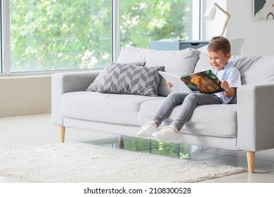 Cute little boy with reading book on sofa in living room - Powered by Shutterstock