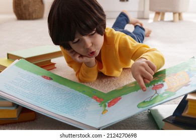 Cute little boy reading book on floor at home - Shutterstock ID 2124270698
