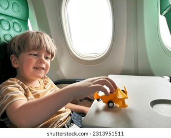 Cute little boy sit near window in the plane playing with toy airplane and smile on the table - Powered by Shutterstock