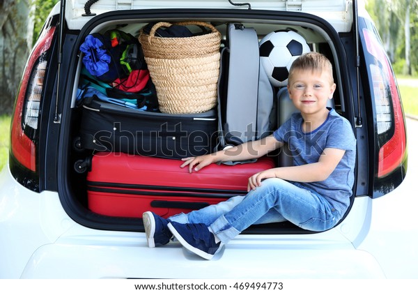 Cute little\
boy sitting in car trunk full of\
bags
