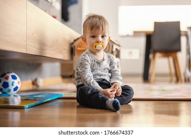 Cute little boy sitting at home with pacifier in his mouth.