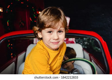 Cute Little Boy Sitting On Red Christmas Car And Looking At Camera. Child. Christmas Mood. Holidays. Christmas. New Year.