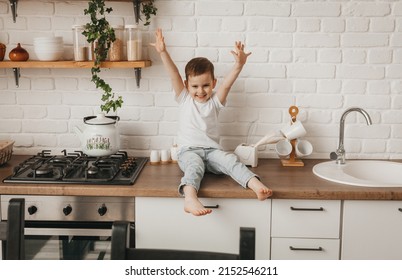 cute little boy sitting on the counter in a stylish kitchen with his bare feet dangling